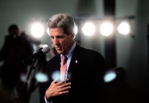 John Kerry speaking, with bright lights behind him (© AP Images)