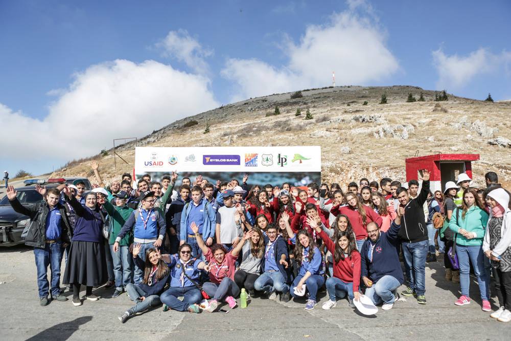 Grupo grande de estudantes acena em frente de faixa; montanha ao fundo (Cortesia: Iniciativa de Reflorestamento do Líbano)