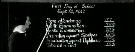 A teacher reviews a classroom's vaccination status on a blackboard.