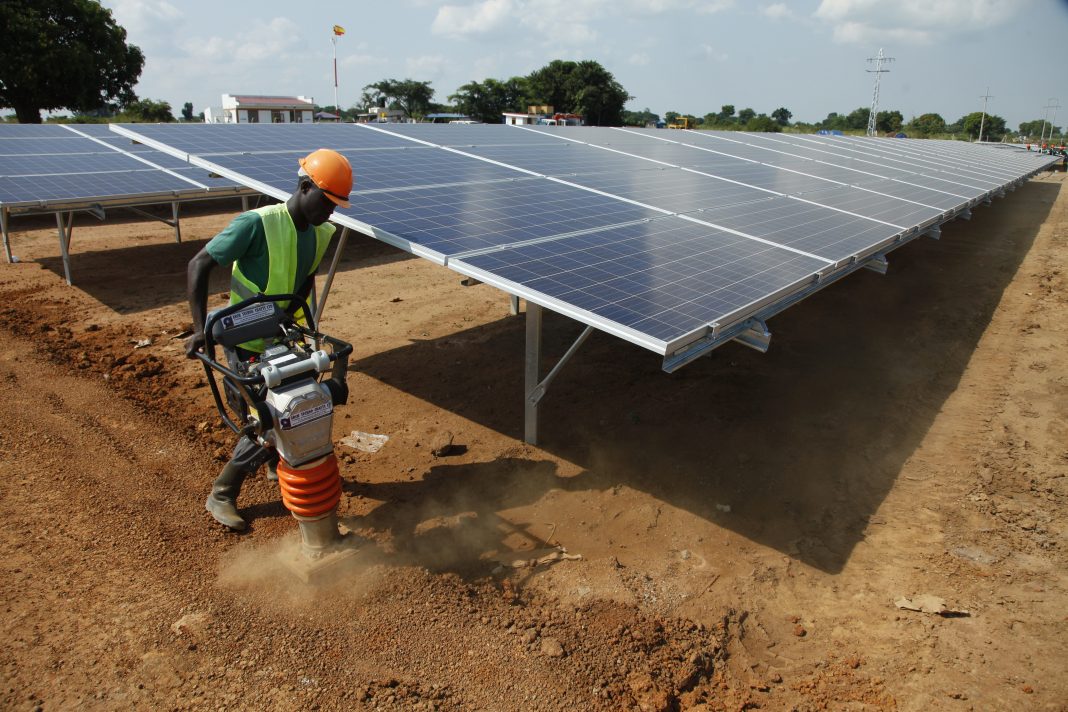 Worker in hard hat operating power tamper next to solar panel array (© AP Images)