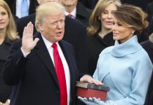 O presidente Trump com uma mão levantada e outra na Bíblia que é segurada por Melania Trump (© AP Images)