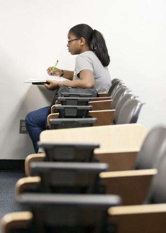 Girl in classroom taking notes at the end of a row of desks