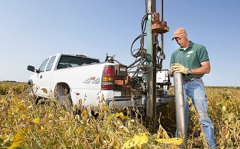 U.S. Department of Agriculture Agriculture Research Service technician prepares a large core sampler to take a core sample of the wood chip bioreactor beneath a soybean field for lab analysis of denitrification rates and bacterial populations