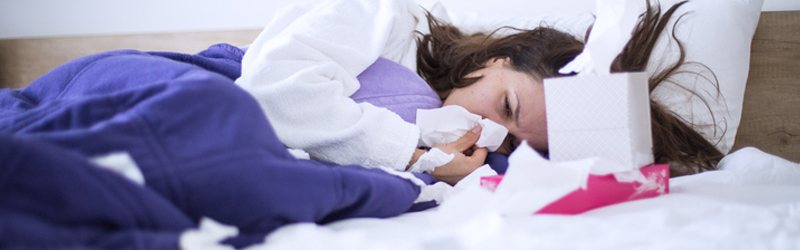 Slider image - Woman huddled in bed covered with tissues blowing her nose