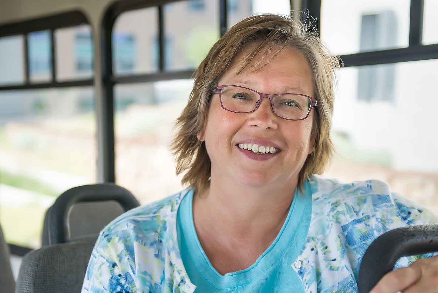 A photo of a woman sitting on a bus, smiling at the camera.