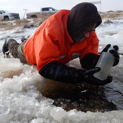 USGS scientist lifting a sample bottle from ice hole 