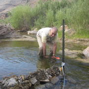 Image shows a man standing ankle-deep in a stream with an orange sampler