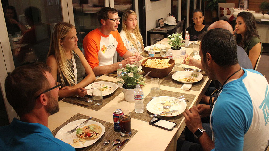 Photo of people sitting around a table eating and talking during a dinner party.