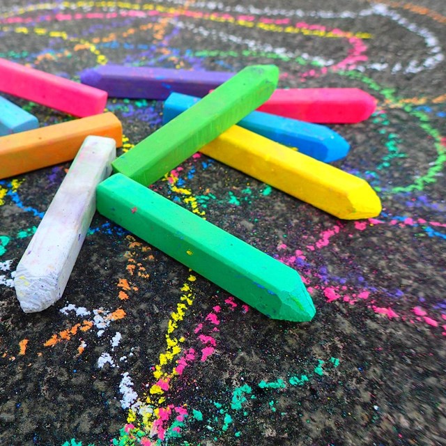 Sticks of different colors of sidewalk chalk on decorated pavement