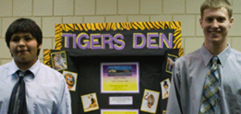 Two young men stand beside a poster.