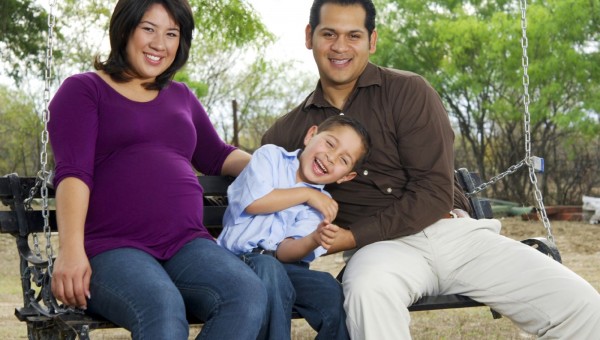 Smiling Hispanic family sitting on a park bench.