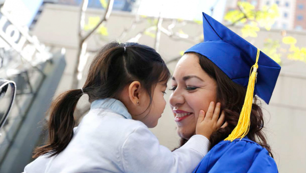 Smiling woman in graduation cap holding a young girl