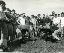 Original Caption: Football training has begun at constabulary headquarters at Bamberg, Germany. Practicing blocking are, Left to Right, Pfc, Bernard Clark of Sleepeye, Minn., and Pfc. Dang Davison of Downer's Grove, Ill. Coach Sandy Clark, wearing a white shirt, looks on from the rear left. August 20, 1946. Local ID: 111-SC-253147