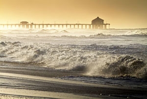 Photo of low waves in the ocean.  A dock is visible in the background.