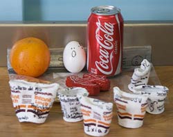 image of crushed styrofoam cups, soda can, an egg, and an orange on a table