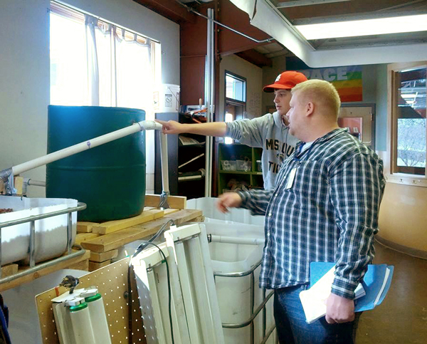 Kris Johnson of the Region 6 Fish & Aquatic Conservation program assists Michael McGimsey with calculations needed to determine the system volume and head pressure in their recirculating aquaculture system. The students in Compass Montessori's aquaponics curriculum needed to add a larger water pump to more effectively raise tilapia and lettuce for the school's kitchen. Credit - Joanne Grady/FWS