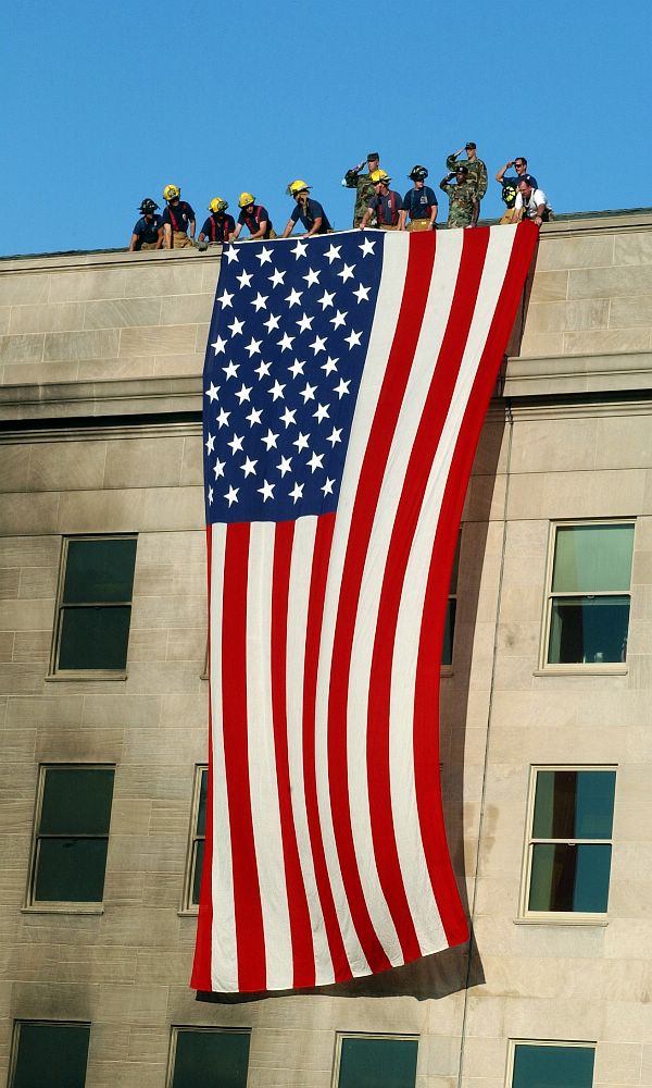 Arlington. Va. (Sept. 12, 2001) -- Military servicemembers render honors as fire and rescue workers unfurl a huge American flag over the side of the Pentagon during rescue and recovery efforts following the Sept 11 terrorist attack. The attack came at approximately 9:40 a.m. as a hijacked commercial airliner, originating from Washington D.C.'s Dulles airport, was flown into the southern side of the building facing Route 27. U.S. Navy photo by Photographer's Mate 1st Class Michael W. Pendergrass.