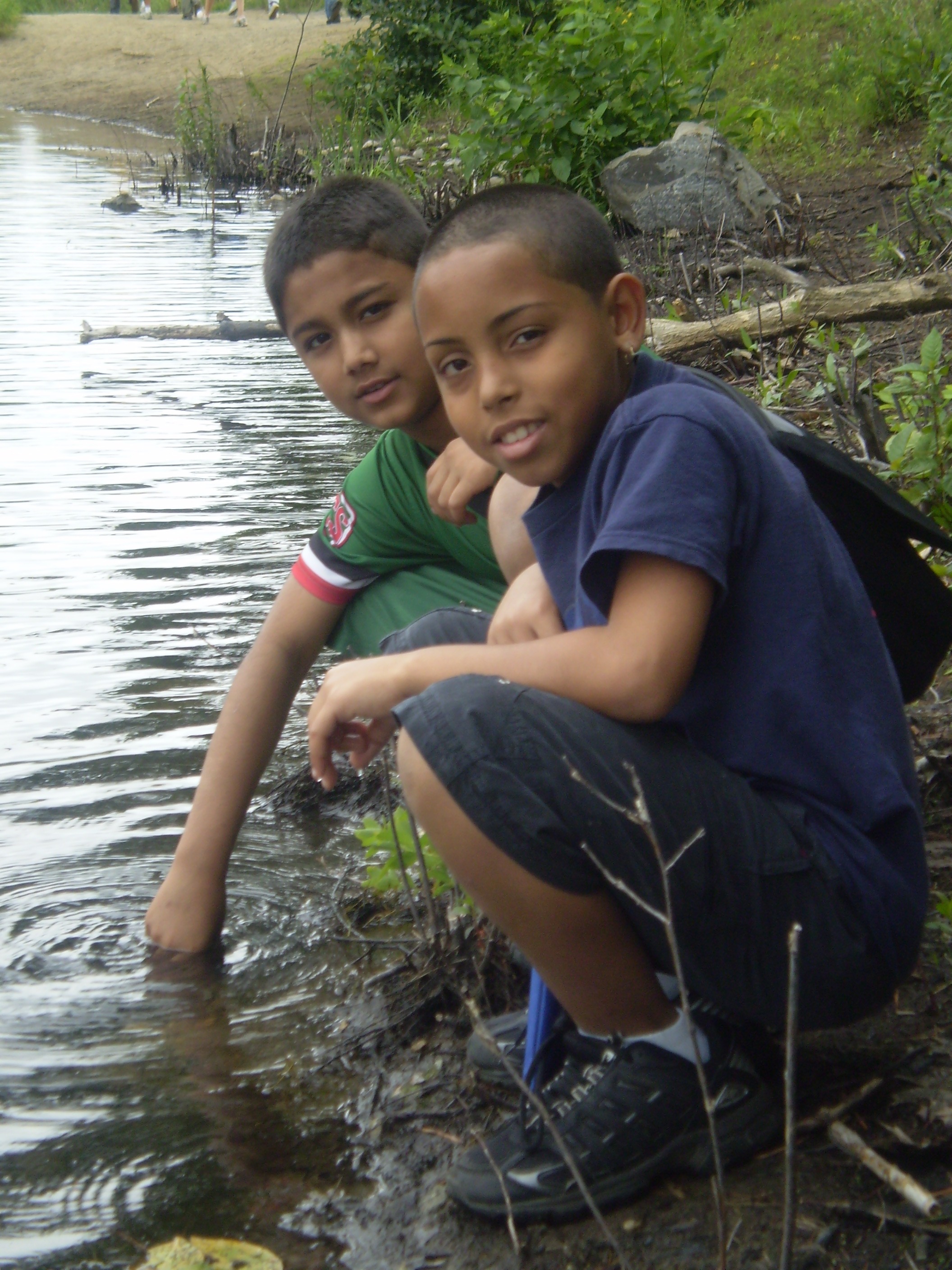 Two young boys kneeling by a body of murky water