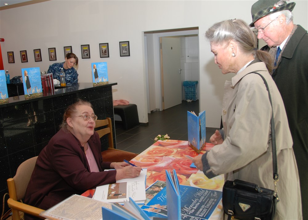 STUTTGART, Germany  -  Mercedes Wild, the child featured in the German-American friendship story  &#34;Mercedes and the Chocolate Pilot,&#34; signs books at the Kelley Theater on Kelley Barracks October 13, 2010. The event was part of the U.S. Africa Command (AFRICOM) Educational Outreach Program. Wild shared her experience as a child during the Berlin Airlift in 1948 and of U.S. Air Force pilot Colonel Gail Halverson, who dropped thousands of tons of candy into the hands of German children.  Wild will also be featured in the Tell Me a Story program at Robinson Barracks where children will be introduced to living history October 14, 2010.