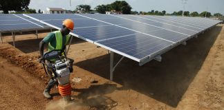 Worker in hard hat operating power tamper next to solar panel array (© AP Images)