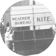 A weather kite being prepared for launching with kite-reel house in the background.