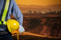 A miner wearing safety gear stands in front of an active work site.