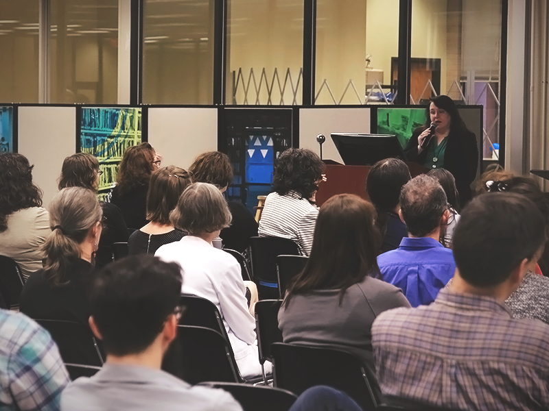 woman standing at a presentation stand speaking to a group of people