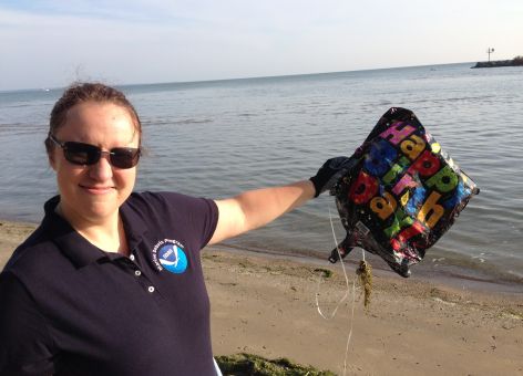 A woman on a beach holding a deflated "Happy Birthday" balloon.