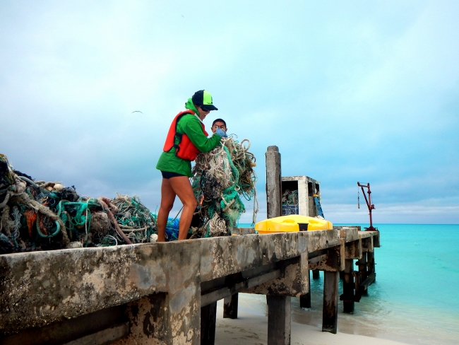 Working alongside DLNR staff, Liat and Ryan remove derelict fishing nets collected on the pier at Kure and eliminate entanglement hazards.