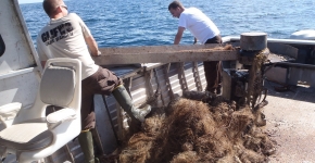 Two people hauling a derelict net onto a boat.