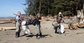 Three people carrying marine debris off a beach.