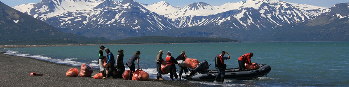 Volunteers loading debris into a boat on a remote Alaskan shoreline. 