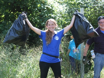 A volunteer smiling and holding up two bags of collected debris.