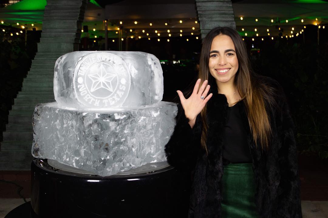 UNT student smiling in front of the University of North Texas Ring ice sculpture. 