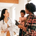 Infant and female caregiver holding tablet and speaking with doctor.