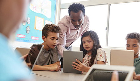 Image of teacher working with young students on iPads