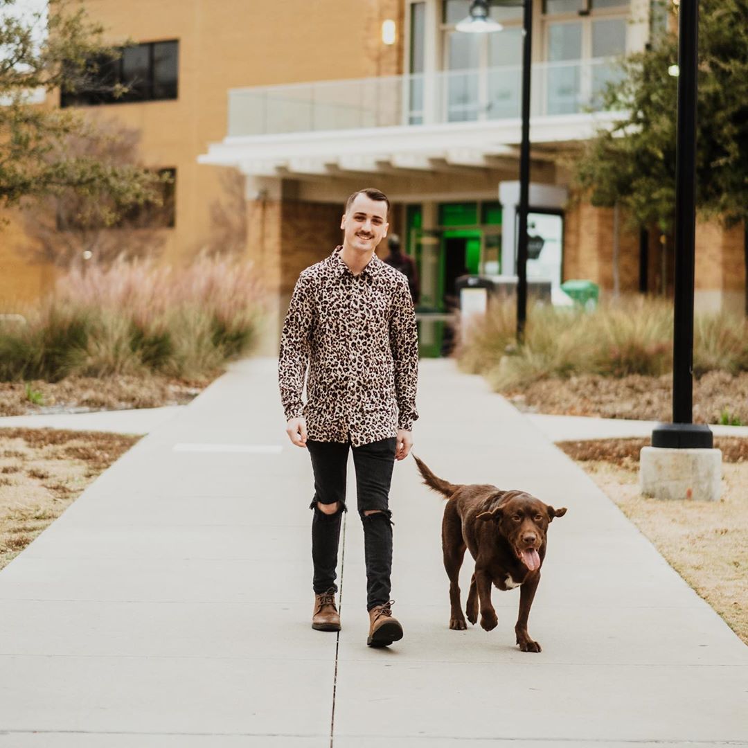 Student walking with his brown lab in front of the UNT Union.