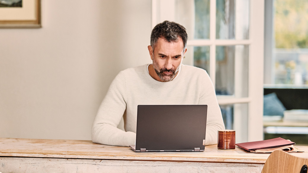 Man uses a laptop computer at home while seated at a long wooden table