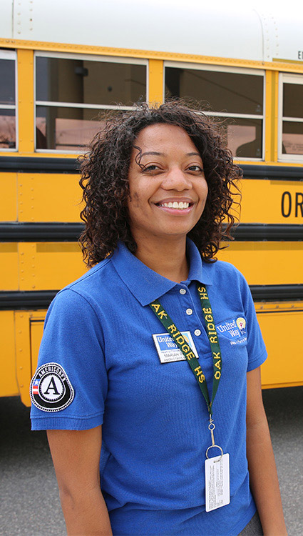 AmeriCorps State & National Member working with United Way in front of school bus. 