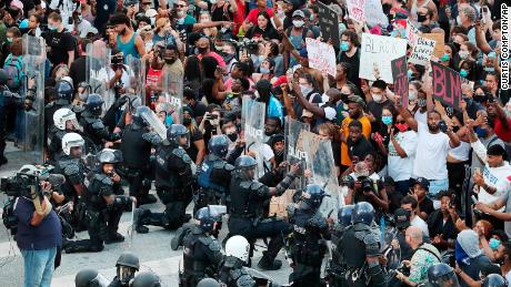 In a show of peace and solidarity, law enforcement officials with riot shields kneel in front of protesters Monday, June 1, 2020, during a fourth day of protests over the death of George Floyd in Minneapolis. (Curtis Compton/Atlanta Journal-Constitution via AP)