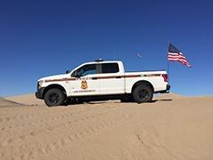 A law enforcement truck with an American flag parked on a sand dune