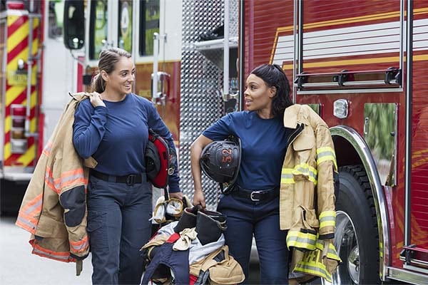 two firefighters carrying gear and talking