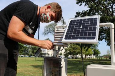 Young man with face mask standing over sensor with solar panel on grassy lawn