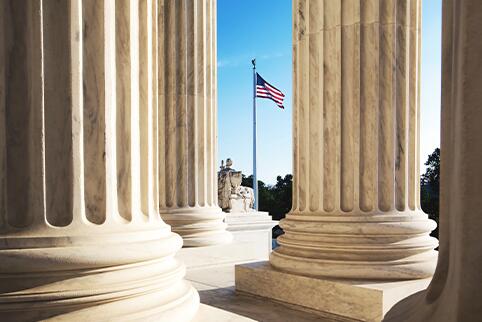 Columns of a building and in between you see an American Flag waving in the breeze