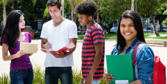 3 teens looking at papers with a fourth teen smiling in foreground