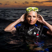 A woman in scuba gear emerges from the surface of the water at dusk