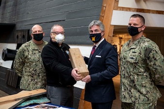 Secretary of the Navy Kenneth J. Braithwaite, second from right, donates a Georgia pine timber fragment from the heavy frigate USS Chesapeake to the National Museum of the U.S. Navy during an artifact presentation.