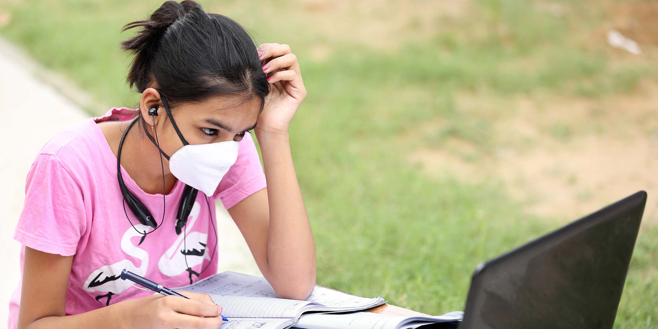 Photo of female student wearing a mask working outdoors on a laptop
