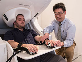 Dr. Mingxiong Huang prepares to do a MEG brain scan on a “healthy control” who has participated in his neuroimaging research. (Photo by Kevin Walsh) 