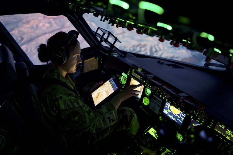 An airman sits in a cockpit illuminated by green light.